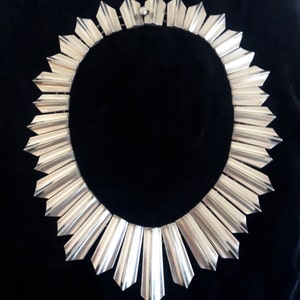 May include: A silver necklace with a geometric design. The necklace is made of many small, pointed pieces that are arranged in a circle. The necklace is a statement piece that would be perfect for a special occasion.
