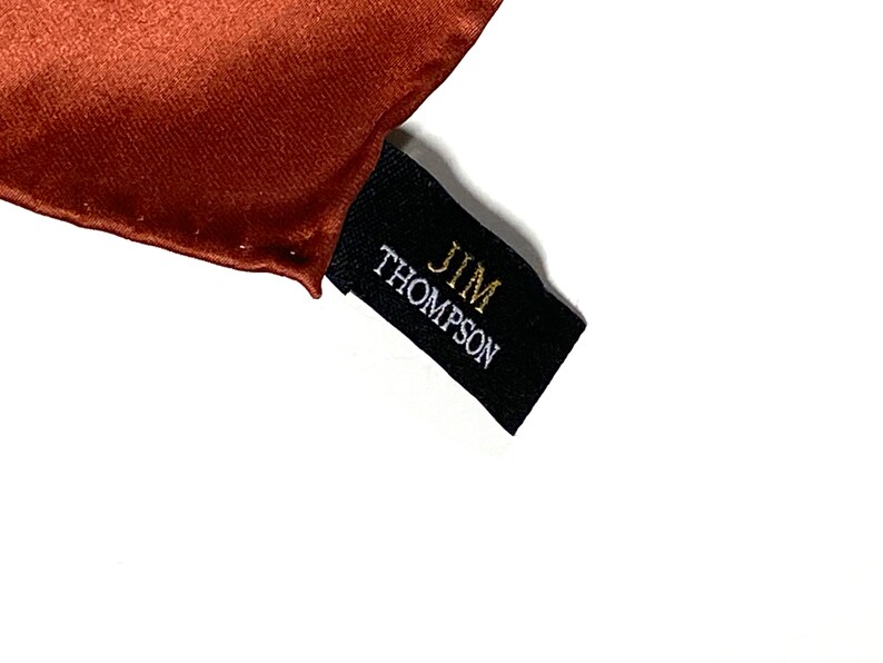 May include: A black fabric label with the text "JIM THOMPSON" in gold and white lettering.