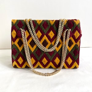 May include: A small, rectangular purse with a geometric pattern in shades of red, yellow, and green. The purse has a gold chain strap.
