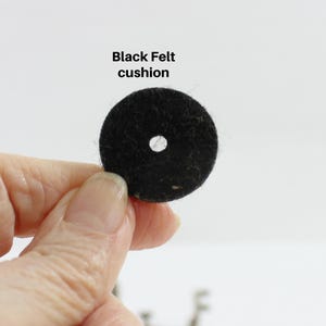 May include: A black felt cushion with a central hole. The text "Black Felt cushion" is displayed above the cushion. The cushion is round and made of a dark, textured material.