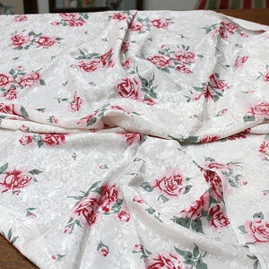 May include: White fabric with a floral pattern of pink and red roses. The fabric is draped and folded.