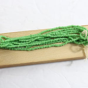 May include: A strand of light green seed beads on a wooden surface. The beads are small and uniform in size.