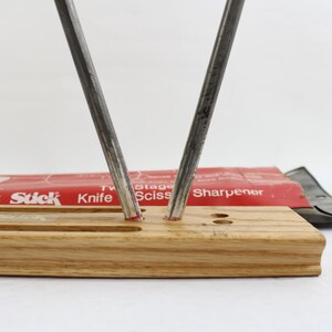 May include: A knife and scissor sharpener with a wooden base. Two steel rods are angled upwards. The red packaging reads "Crock Stick Knife Sciss Sharpener". A black scissor sharpener is also visible.