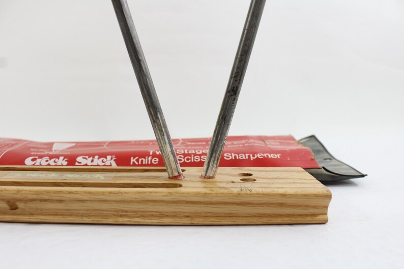 May include: A knife and scissor sharpener with a wooden base. Two steel rods are angled upwards. The red packaging reads "Crock Stick Knife Sciss Sharpener". A black scissor sharpener is also visible.