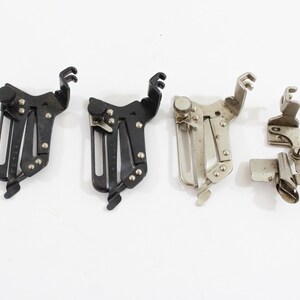 May include: Four vintage sewing machine attachments are displayed against a white background. Two are black, and two are silver-toned. The attachments have various shapes and designs, including levers, screws, and slotted sections.
