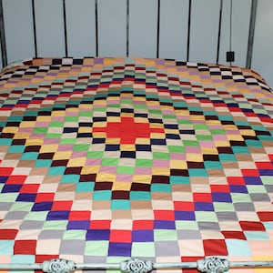 May include: A bed quilt featuring a multi-colored patchwork design arranged in a concentric diamond pattern. The quilt is composed of numerous small square fabric patches in various solid colors including red, blue, green, yellow, and purple.