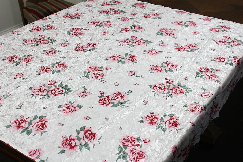 May include: White tablecloth with a repeating pattern of pink roses with green leaves.