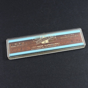 May include: A rectangular, clear plastic case containing Koh-I-Noor Rapidoguides. The case has a light blue and brown label with text including "Koh-I-Noor" and "Rapidoguides". The case is on a dark surface.