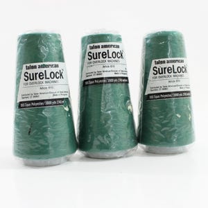 May include: Three spools of green SureLock thread for overlock machines. Each spool is wrapped in clear plastic and has a white label with black text. The labels read "SureLock" and "100% Spun Polyester/3000 yds 2743 m".