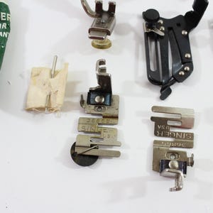 May include: Assortment of vintage sewing machine parts, including presser feet and a tube of Singer motor lubricant. The lubricant tube is green with white text. The presser feet are silver and black.