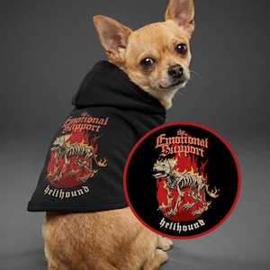 May include: A small dog wearing a black hoodie with the text "the Emotional Support" and "hellhound" in a gothic font. The hoodie features a graphic of a dog skeleton engulfed in flames. A circular patch with the same design is also visible.