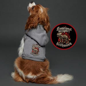 May include: A Cavalier King Charles Spaniel wearing a gray hoodie with the words "Emotional Support Hellhound" printed on the back. A matching circular patch with the same design is visible.