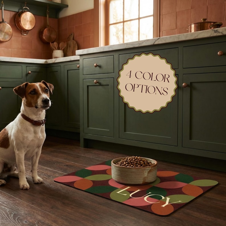 May include: A Jack Russell Terrier sits near a patterned dog food mat with the name "LUCY" on it. A ceramic bowl filled with dog food sits on the mat. The mat has a geometric design in shades of red, green, and orange. The text "4 COLOR OPTIONS" is visible.