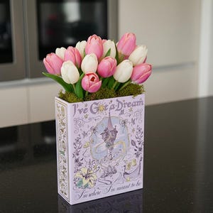 May include: A floral arrangement featuring pink and white tulips in a decorative box. The box is lavender with the text "I've Got a Dream" and a castle illustration. The flowers sit atop green moss, creating a vibrant display.