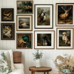 Op de afbeelding: Een verzameling ingelijste dierenschilderijen in vintage-stijl, waaronder een vos, een eend, een hert en honden, tentoongesteld op een witte muur. De kunstwerken hebben gedetailleerde penseelstreken en warme, aardse tinten, waardoor een rustieke esthetiek ontstaat. De kamer omvat ook een witte bank met decoratieve kussens en een houten bijzettafel.