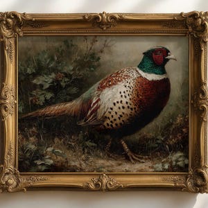 Op de afbeelding: Een schilderij van een fazant in een sierlijke gouden lijst. De vogel heeft een rode kop, groene nek en bruin-witte veren. Het kunstwerk is geplaatst tegen een achtergrond van bladeren.