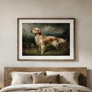 Op de afbeelding: Een ingelijste print van een Golden Retriever in een veld. De hond heeft een lichtgouden kleur en het kunstwerk heeft een vintage stijl. De achtergrond toont een bewolkte lucht en bladeren, in een houten frame.