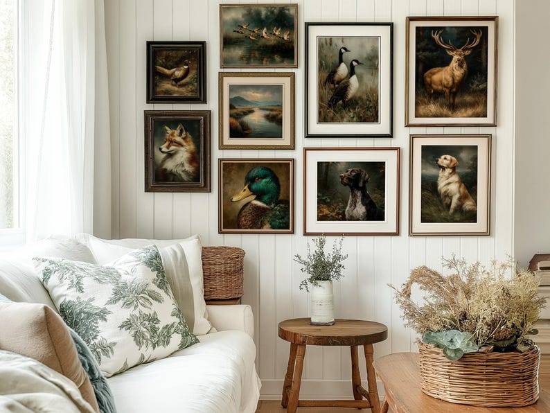 Op de afbeelding: Een verzameling ingelijste dierenschilderijen in vintage-stijl, waaronder een vos, een eend, een hert en honden, tentoongesteld op een witte muur. De kunstwerken hebben gedetailleerde penseelstreken en warme, aardse tinten, waardoor een rustieke esthetiek ontstaat. De kamer omvat ook een witte bank met decoratieve kussens en een houten bijzettafel.