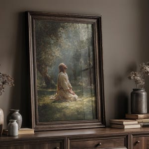 Peut inclure: Une impression d'art religieux encadr&eacute;e repr&eacute;sente une figure agenouill&eacute;e en pri&egrave;re sous un arbre. L'&oelig;uvre est dans un cadre en bois fonc&eacute;, pos&eacute;e sur un meuble en bois fonc&eacute;. Des fleurs s&eacute;ch&eacute;es dans des vases et des livres sont &eacute;galement sur le meuble.