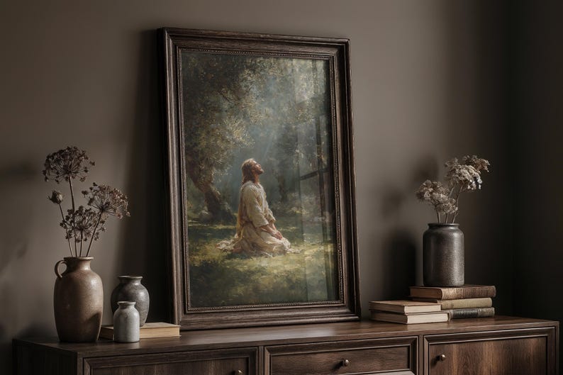 Peut inclure: Une impression d'art religieux encadr&eacute;e repr&eacute;sente une figure agenouill&eacute;e en pri&egrave;re sous un arbre. L'&oelig;uvre est dans un cadre en bois fonc&eacute;, pos&eacute;e sur un meuble en bois fonc&eacute;. Des fleurs s&eacute;ch&eacute;es dans des vases et des livres sont &eacute;galement sur le meuble.