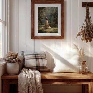 Peut inclure: Une &oelig;uvre d'art encadr&eacute;e repr&eacute;sente une personne agenouill&eacute;e dans une for&ecirc;t ensoleill&eacute;e. L'&oelig;uvre est dans un cadre en bois marron, accroch&eacute;e &agrave; un mur &agrave; panneaux blancs. Un banc en bois contient des coussins, une couverture tricot&eacute;e et des vases d&eacute;coratifs avec des plantes s&eacute;ch&eacute;es.