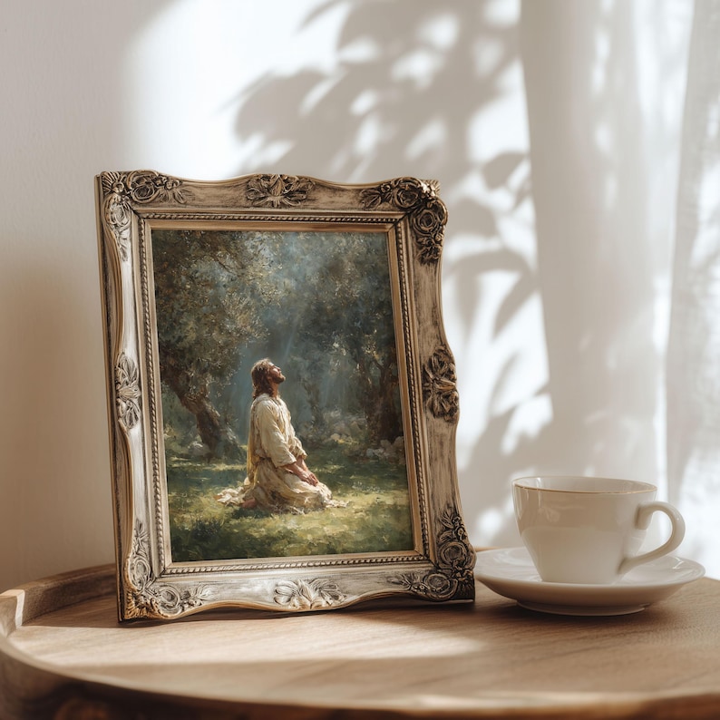 Peut inclure: Une &oelig;uvre d'art religieuse encadr&eacute;e repr&eacute;sente une figure agenouill&eacute;e dans une for&ecirc;t, regardant vers le haut. Le cadre beige orn&eacute; entoure la peinture. Une tasse &agrave; th&eacute; et une soucoupe blanches sont pos&eacute;es sur une surface en bois.