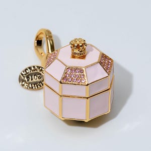 May include: A gold-toned charm shaped like an octagonal box with light pink enamel panels. The lid features a small gold crown finial and pink crystal accents. A gold lobster clasp is attached, along with a round tag engraved with 2014 EDITION.