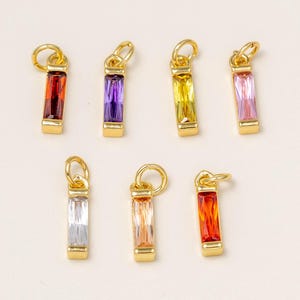 Peut inclure: Sept breloques rectangulaires en pierre taillée en baguette, serties dans des montures en métal doré. Chaque breloque présente une pierre de couleur différente, dont rouge, violet, jaune, rose, transparent, pêche et orange, avec un anneau.