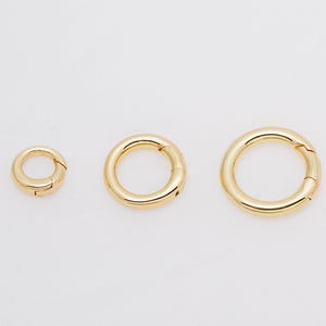 Peut inclure: Trois anneaux ressort circulaires de couleur dorée disposés en rangée du plus petit au plus grand. Chaque anneau présente une finition métallique lisse et polie ainsi qu'un mécanisme à ressort fonctionnel permettant une ouverture sécurisée.