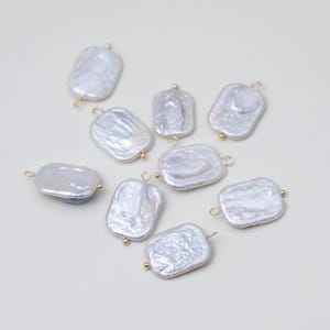 May include: A collection of nine rectangular, iridescent white freshwater pearl charms. Each pearl features a textured, organic surface and is fitted with a small gold-toned metal loop at one or both ends for attachment, showcasing a lustrous finish.