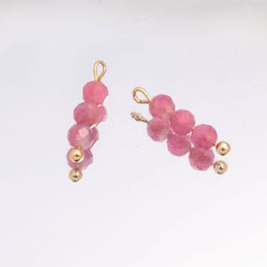 Peut inclure: Deux breloques de bijoux composées d'un arrangement vertical de perles roses à facettes et de petites sphères en métal doré. Chaque breloque est fixée à une boucle en fil doré sur le dessus, conçue pour être suspendue à un bijou plus grand.