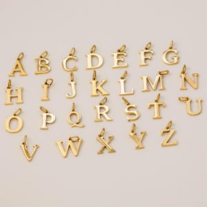 Peut inclure: Une collection de vingt-six breloques individuelles en métal doré, chacune dotée d'un petit anneau de jonction sur le dessus. Les lettres de l'alphabet sont disposées en rangées, présentant une finition polie et une police à empattement classique.