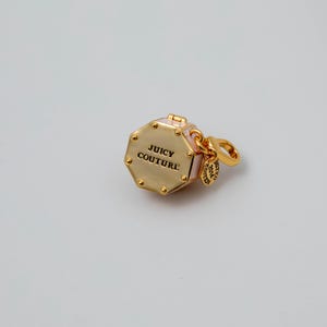 May include: A gold-tone metal charm shaped like an octagon with light pink enamel sides. The top surface features the text JUICY COUTURE in black lettering. A small round tag attached to the jump ring is engraved with LIMITED EDITION 2014.
