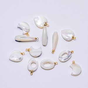 May include: A collection of white mother-of-pearl charms in various shapes including crescents, teardrops, hearts, and rings. Each piece features a polished iridescent surface and is attached to a small gold-toned metal jump ring for hanging.