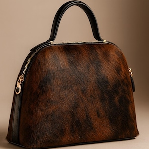 Pode incluir: Bolsa em forma de c&uacute;pula com exterior estampado em castanho e preto. A bolsa apresenta uma al&ccedil;a e acabamentos em couro preto, com z&iacute;per e ferragens douradas. Design estruturado.