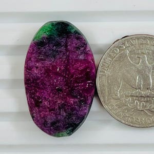 Könnte beinhalten: Ein ovaler Edelstein mit tiefroten und grünen Farbtönen, neben einer US-Vierteldollarmünze. Der Edelstein hat eine strukturierte Oberfläche, und die Münze zeigt ein Adlerdesign.
