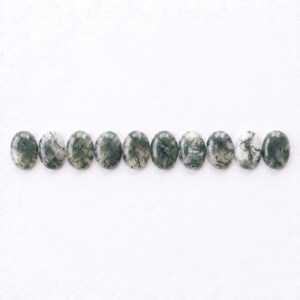 Pu&ograve; includere: Undici cabochon di agata muschiata di forma ovale disposti in una fila orizzontale. Ogni pietra presenta una superficie liscia e lucida con inclusioni naturali uniche di motivi verde scuro, verde bosco e bianco che ricordano il muschio.