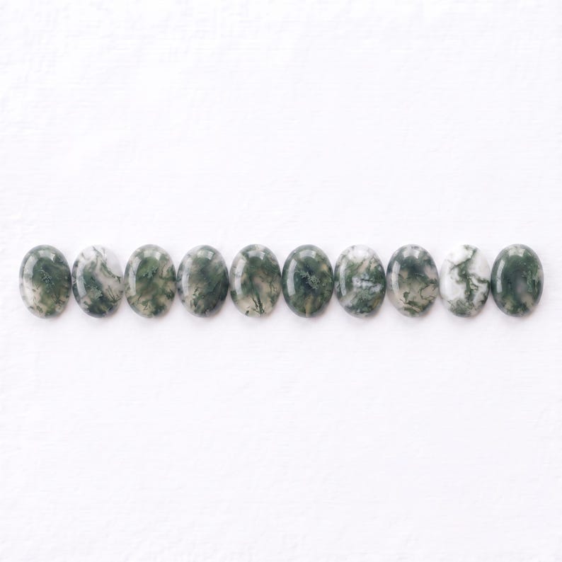 Pu&ograve; includere: Undici cabochon di agata muschiata di forma ovale disposti in una fila orizzontale. Ogni pietra presenta una superficie liscia e lucida con inclusioni naturali uniche di motivi verde scuro, verde bosco e bianco che ricordano il muschio.