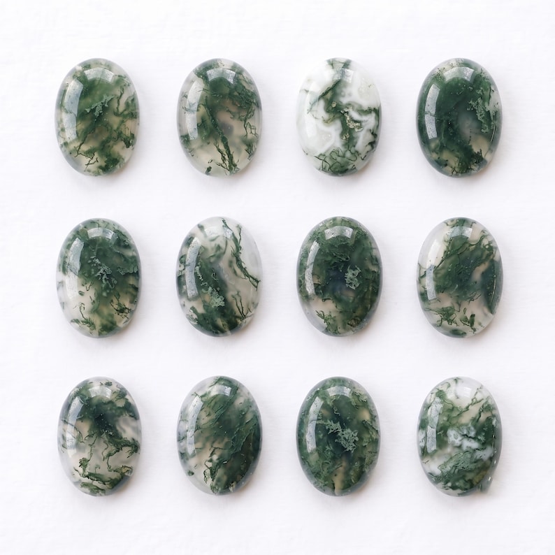Pu&ograve; includere: Dodici cabochon di agata muschiata di forma ovale disposti in una griglia. Ogni pietra presenta una superficie lucida e liscia con colori di base bianco traslucido e lattiginoso contenenti intricate inclusioni dendritiche verde scuro.