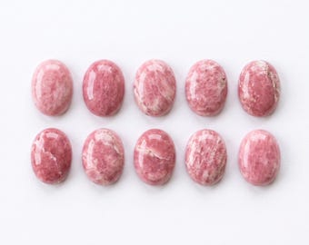 Può includere: Dieci cabochon di rodonite di forma ovale disposti in due file da cinque. Ogni pietra presenta una superficie lucida e liscia con un motivo distinto di inclusioni minerali screziate rosa e bianche, che mostrano variazioni naturali di colore.