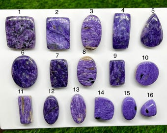 Può includere: Sedici cabochon di charoite lucidati in varie forme, tra cui ovali, rettangolari e a goccia. Ogni pietra viola presenta motivi vorticosi unici e inclusioni nere, numerate da uno a sedici su una superficie bianca.