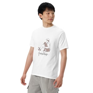 Peut inclure: T-shirt blanc avec un dessin au trait d'une personne et d'un chien, et le mot "friendship" en cursive. L'illustration est dans les tons marron. Le t-shirt a un col rond.