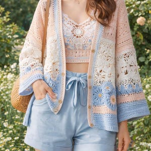 May include: A pastel-colored crochet cardigan with a matching crop top and light blue shorts. The cardigan features a floral design with pink, white, and blue accents. The outfit is completed with a straw bag.