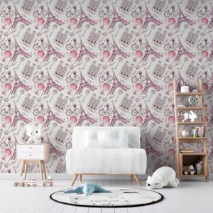 Könnte beinhalten: Ein Zimmer mit Tapeten mit rosa Illustrationen des Eiffelturms, Fahrrädern und anderen Pariser Motiven. Das Zimmer umfasst einen weißen Stuhl, einen Beistelltisch, einen Teppich und ein Holzregal mit dekorativen Gegenständen.