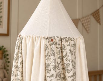 Può includere: Un baldacchino in tessuto sospeso con una sezione superiore conica in crema tinta unita e una sezione inferiore arricciata con pannelli alternati in crema tinta unita e tessuto crema stampato con un motivo botanico a foglie verde scuro.