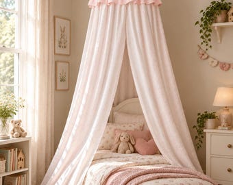 Può includere: Un baldacchino da letto montato a soffitto con una parte superiore a balze rosa tenue e lunghi pannelli in tessuto bianco testurizzato che scendono fino al pavimento, creando un recinto drappeggiato sopra un letto con biancheria floreale e una coperta in maglia rosa.