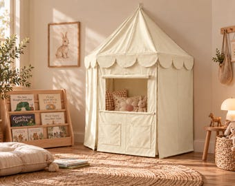 Può includere: Una tenda da gioco in tessuto color crema con tetto a punta e bordo smerlato, una finestra quadrata e due tasche portaoggetti inferiori. L'interno contiene un cuscino a quadri, un cuscino a forma di fiore e un piccolo peluche.