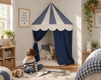 Può includere: Una tenda da gioco angolare con tetto conico a quadri vichy blu navy e bianchi, bordo smerlato e tende blu navy a tinta unita. L'interno contiene un tappetino rotondo con bordo a pompon, un cuscino a forma di nuvola e uno a forma di stella.