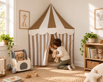 Può includere: Una tenda da gioco angolare con un design in tessuto a righe marroni e bianche e una mantovana smerlata. La tenda presenta un tetto a punta e strisce verticali sulle pareti. La struttura è posizionata in un angolo della stanza.