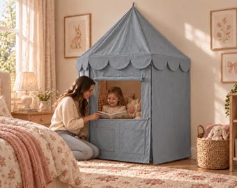 Può includere: Una tenda da gioco in tessuto color blu polvere con tetto conico dai bordi smerlati, un'apertura a finestra quadrata e due tasche rettangolari sul pannello frontale inferiore, progettata per l'uso in ambienti interni.